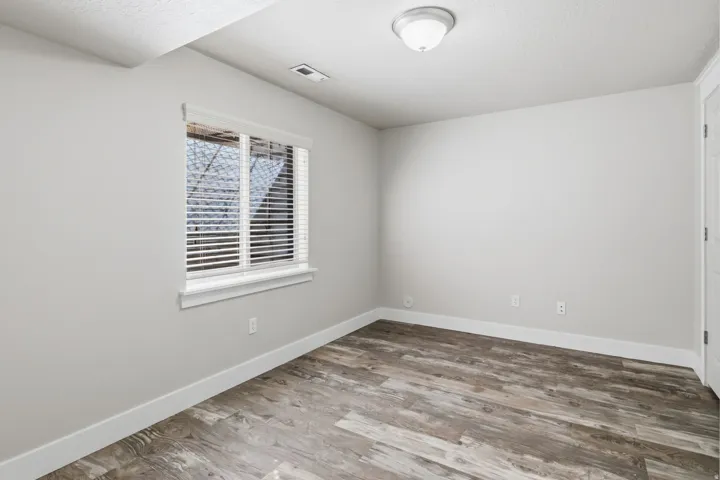 Wood-finish flooring, white trim, and a window with blinds