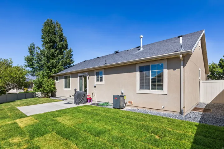 Expansive lawn with a concrete patio, stucco exterior, and dark shingle roof