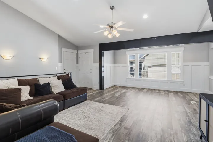 Vaulted ceilings, wood-finish flooring, wainscoting, and a ceiling fan with integrated lighting