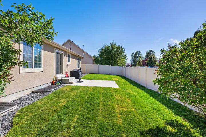 Expansive backyard featuring a lush lawn, concrete patio, sliding glass door, and privacy fencing