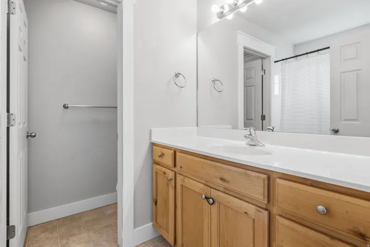Wood-finish vanity with a white countertop, undermount sink, and polished chrome faucet