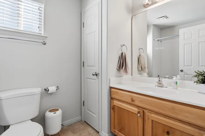 Bathroom featuring a wood-finish vanity with a white countertop and integrated sink, a large wall-mounted mirror, and a white toilet