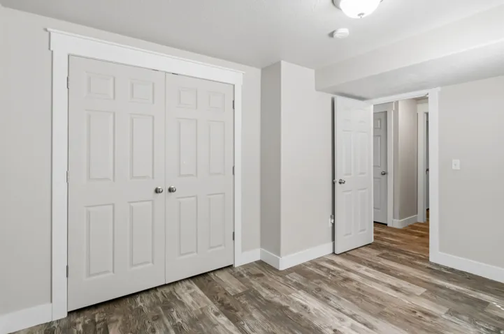 White paneled bi-fold closet doors, wood-finish flooring, white trim, and a flush mount ceiling light
