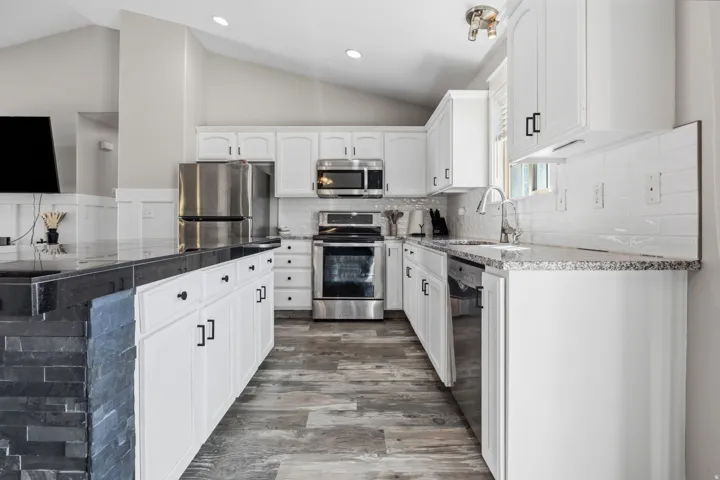 Kitchen featuring white cabinetry with dark hardware, granite countertops, stainless steel appliances, wood-finish flooring, and a stone-clad island