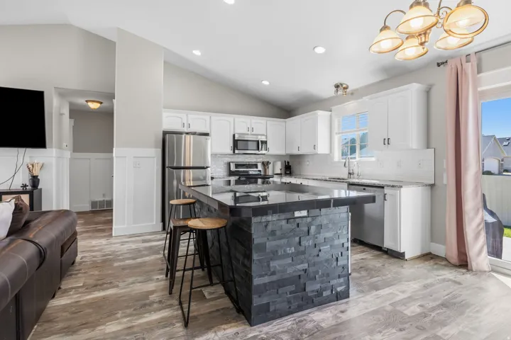 Kitchen featuring an island with a stacked stone finish, white cabinetry, stainless steel appliances, and wood-finish flooring