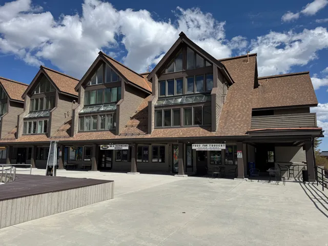 Multi-level commercial facade with multiple storefronts, gabled rooflines, and a spacious concrete patio
