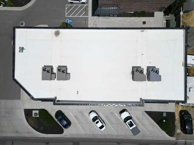 White flat roof with multiple HVAC units and adjacent paved parking
