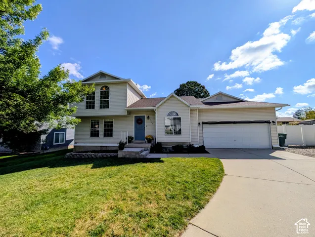 Exterior featuring siding, a two-car garage, a concrete driveway, and a front lawn with mature landscaping