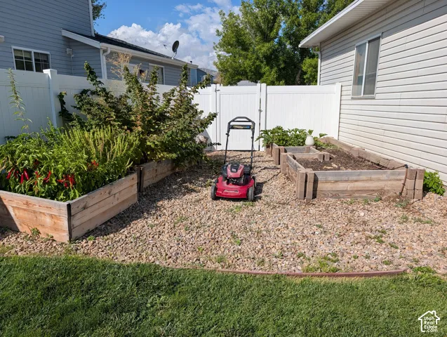 Backyard featuring raised garden beds, gravel ground cover, and a white privacy fence