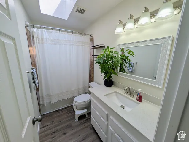 Skylight, wood-finish flooring, white vanity with integrated sink, brushed nickel faucet, and a four-light vanity fixture