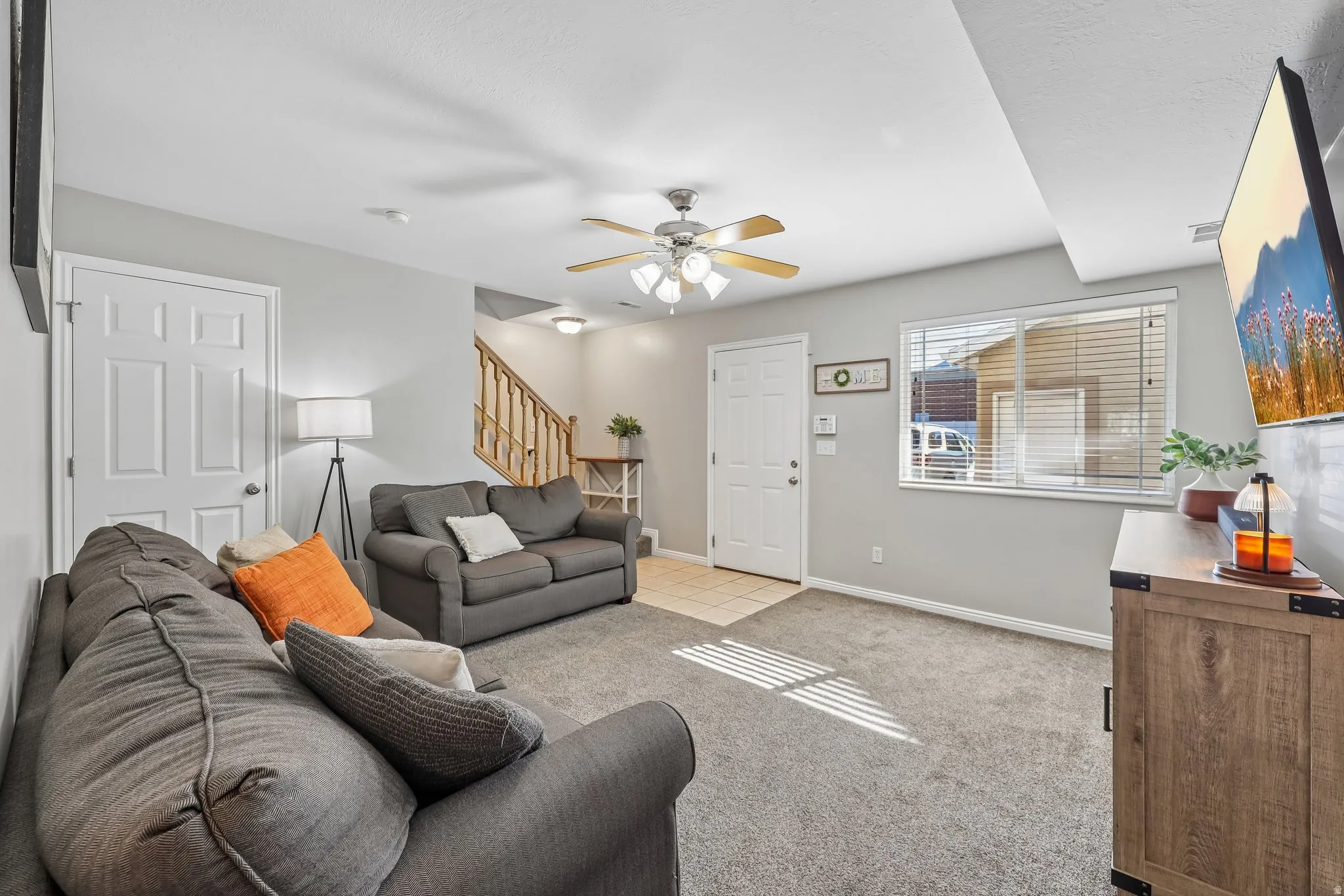 Carpeted living area with light gray walls, a ceiling fan with integrated lighting, and a white paneled door
