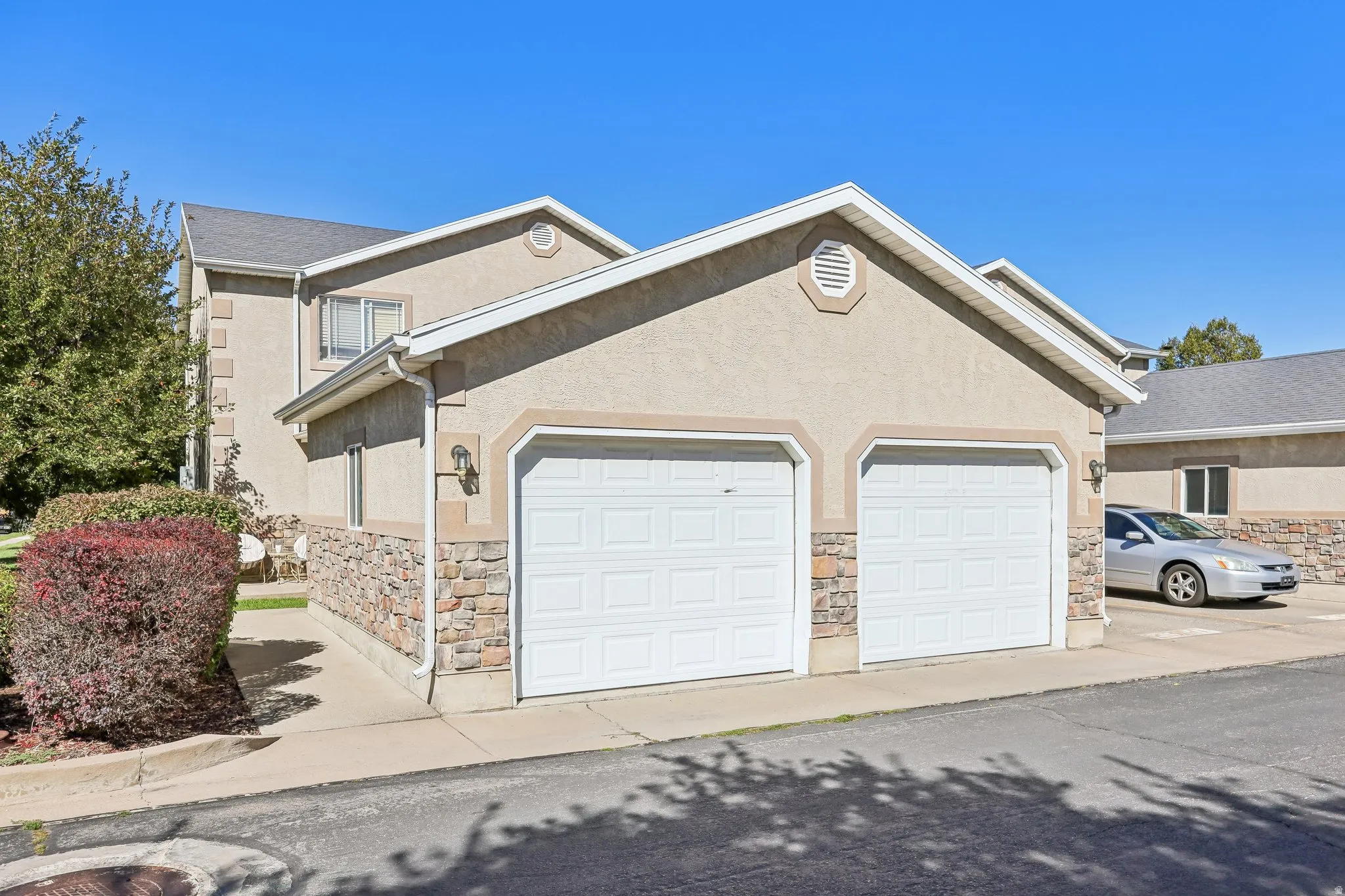 Stucco exterior with stone veneer accents, two-car garage, and gable roof