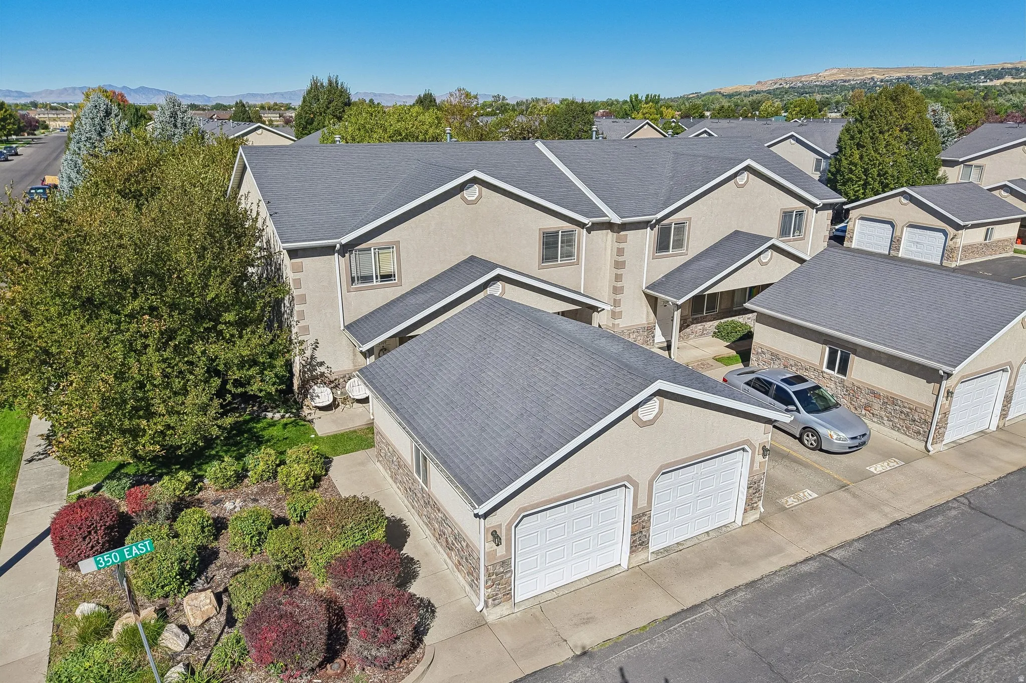 Stucco exterior with stone accent detailing, dual-panel garage doors, and mature landscaping