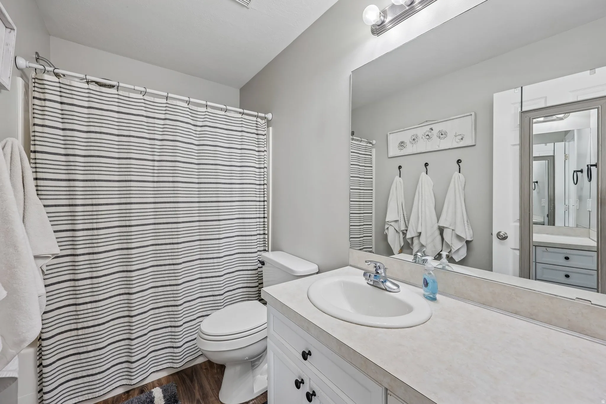 Bathroom featuring a single vanity with an integrated sink, broad wall-mounted mirror, and wood-finish flooring