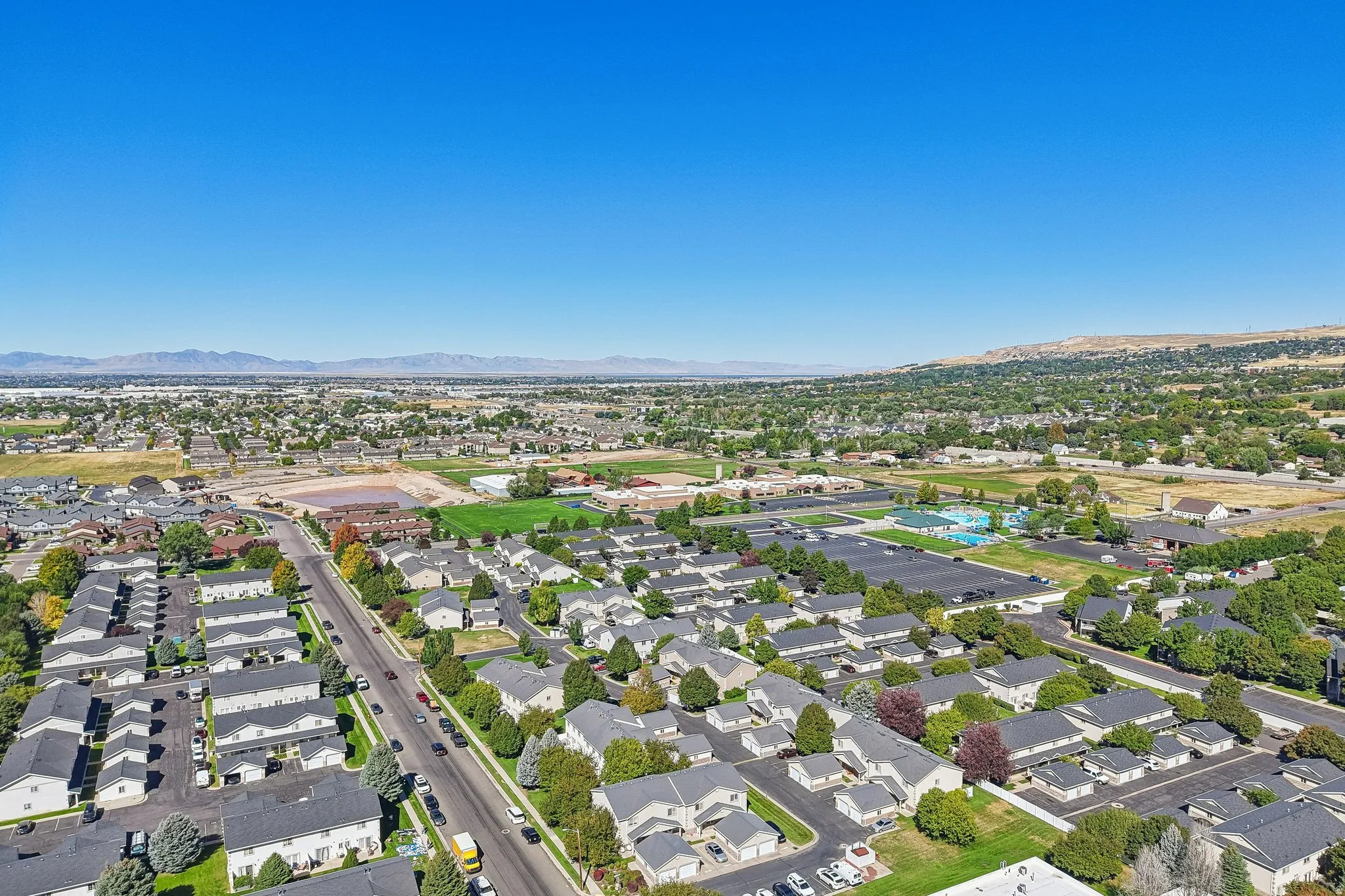 Expansive residential area with a prominent road, featuring a distant mountainous backdrop and a visible pool facility