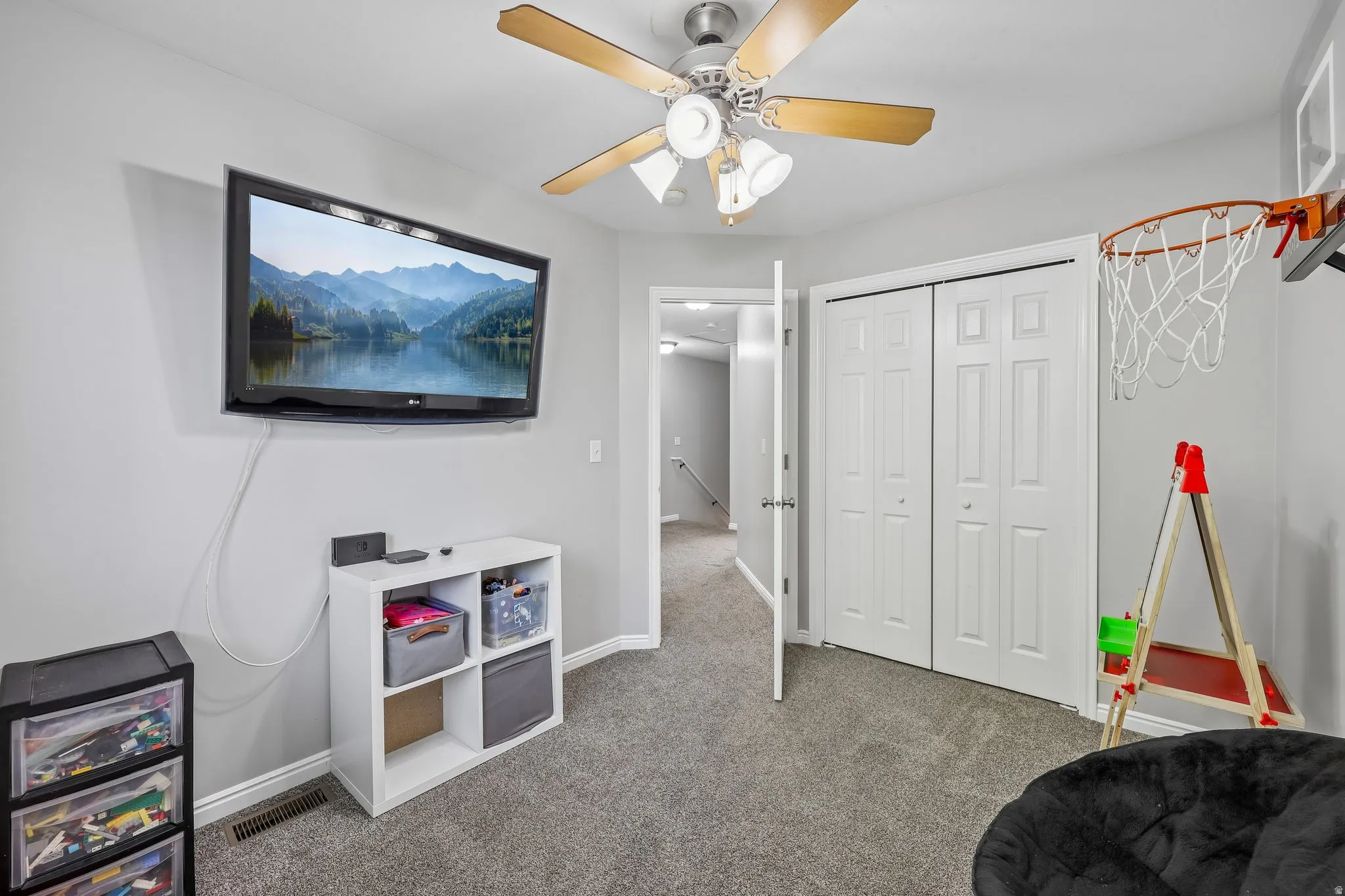 Gray carpeting with a ceiling fan, wall-mounted television, and white bi-fold closet doors