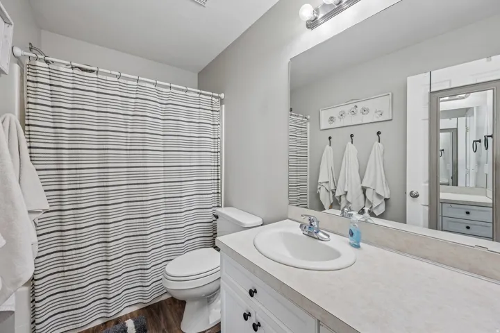 Bathroom featuring a single vanity with an integrated sink, broad wall-mounted mirror, and wood-finish flooring