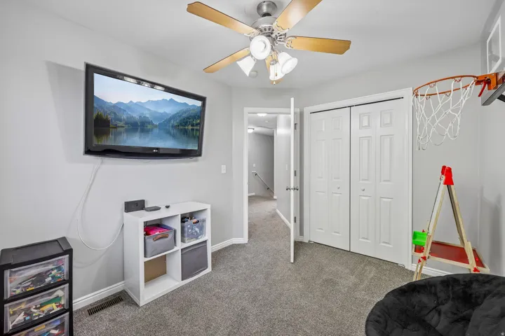 Gray carpeting with a ceiling fan, wall-mounted television, and white bi-fold closet doors