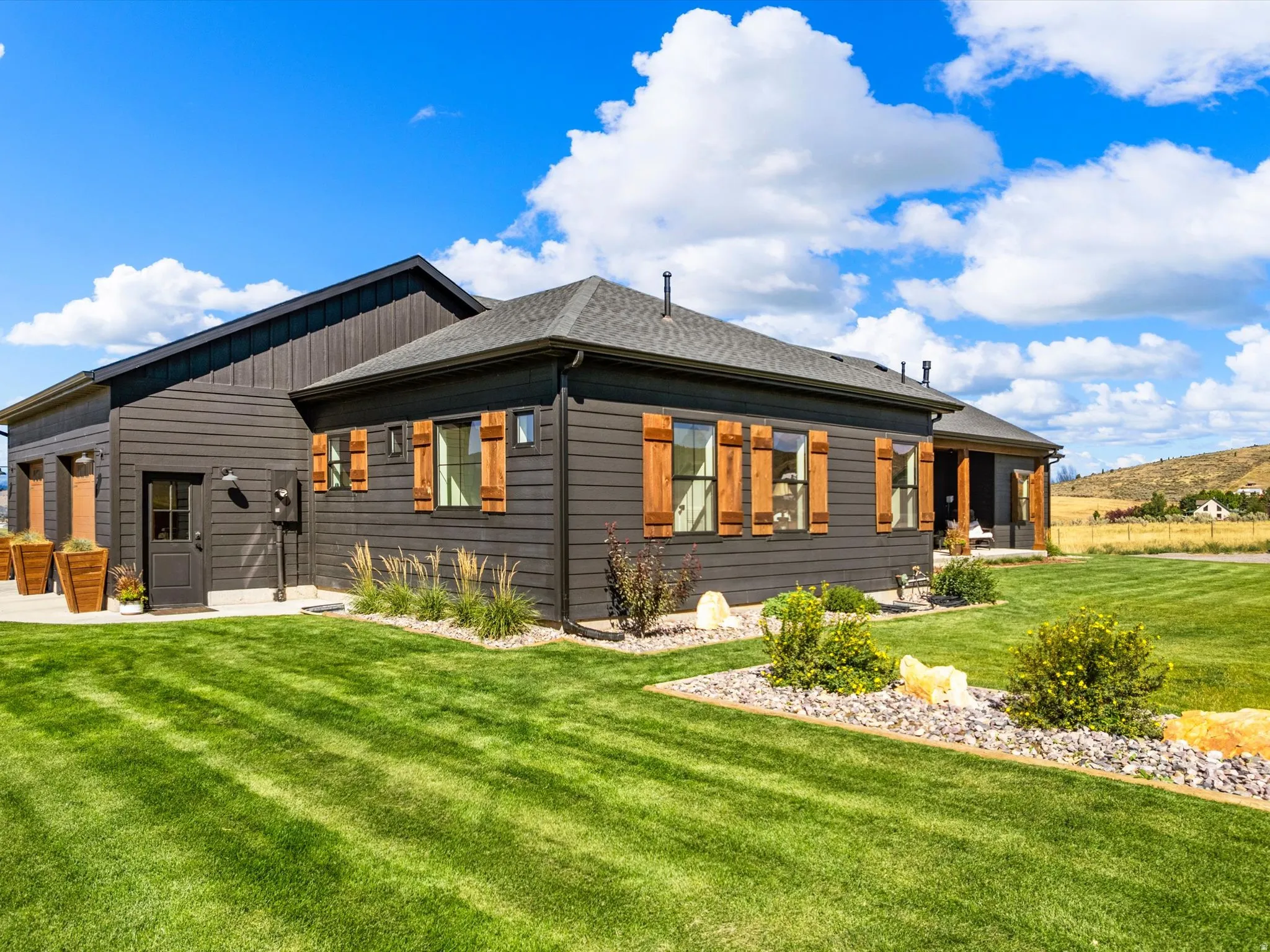 Dark-stained horizontal siding, wood shutters, landscaped garden beds, and a covered porch