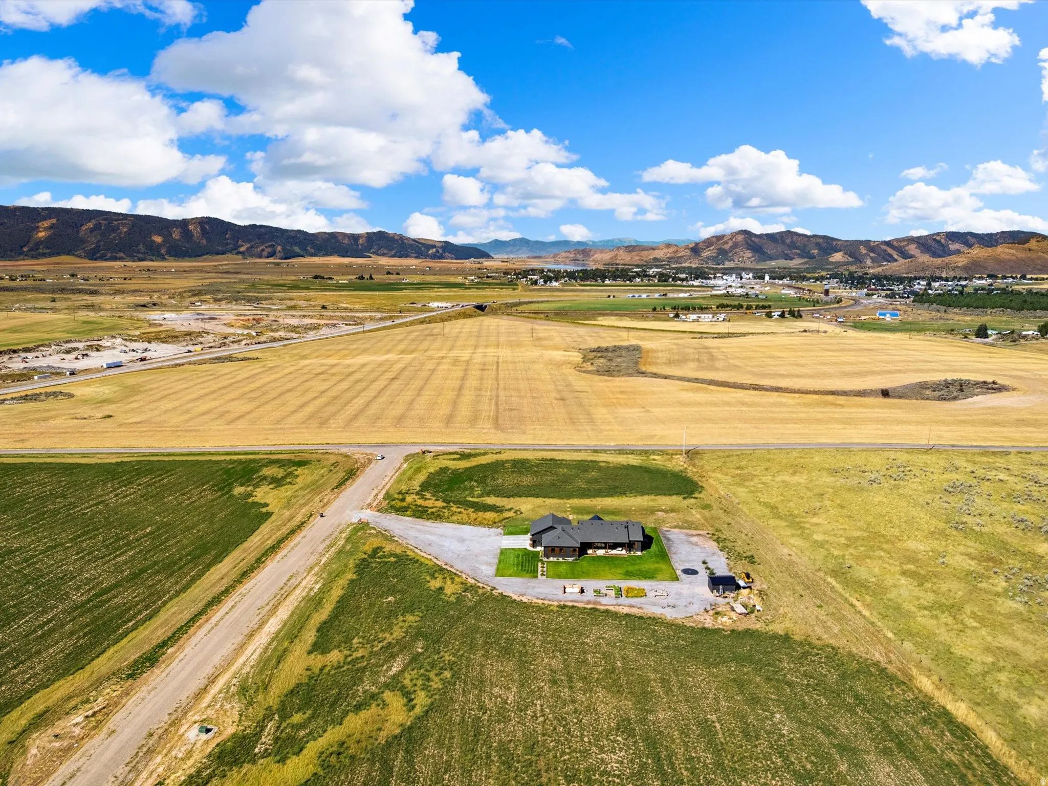 Expansive rural property featuring a single-story residence, gravel driveway, manicured lawn, and surrounding agricultural fields
