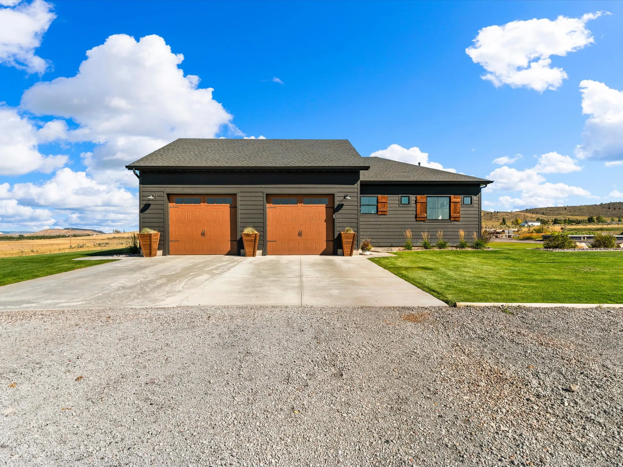 Exterior featuring dark gray siding, a two-car garage with wood-finish doors, a concrete driveway, and a manicured lawn
