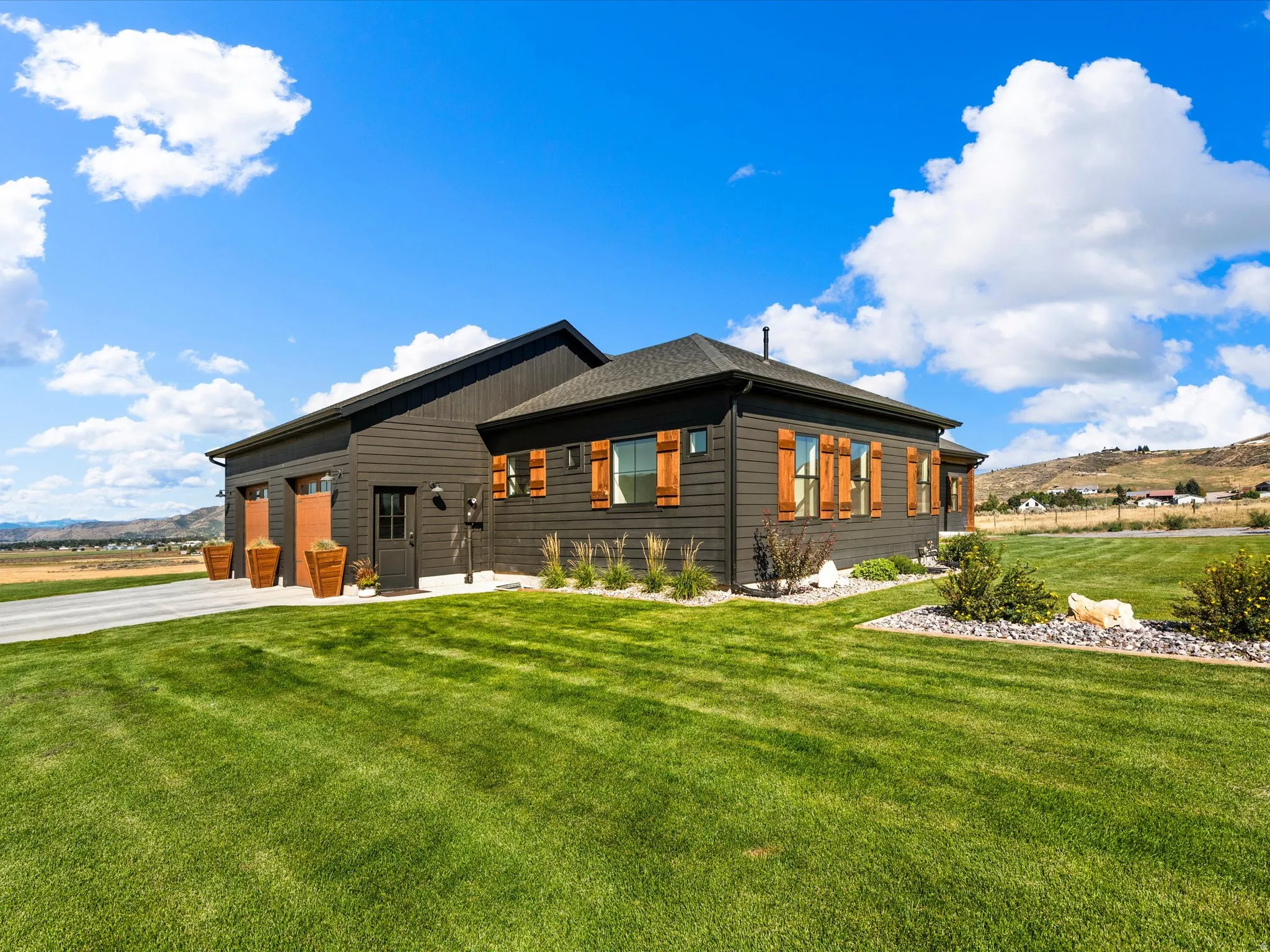 Dark-toned exterior siding with wood-tone window shutters, a two-car garage, and a gravel driveway