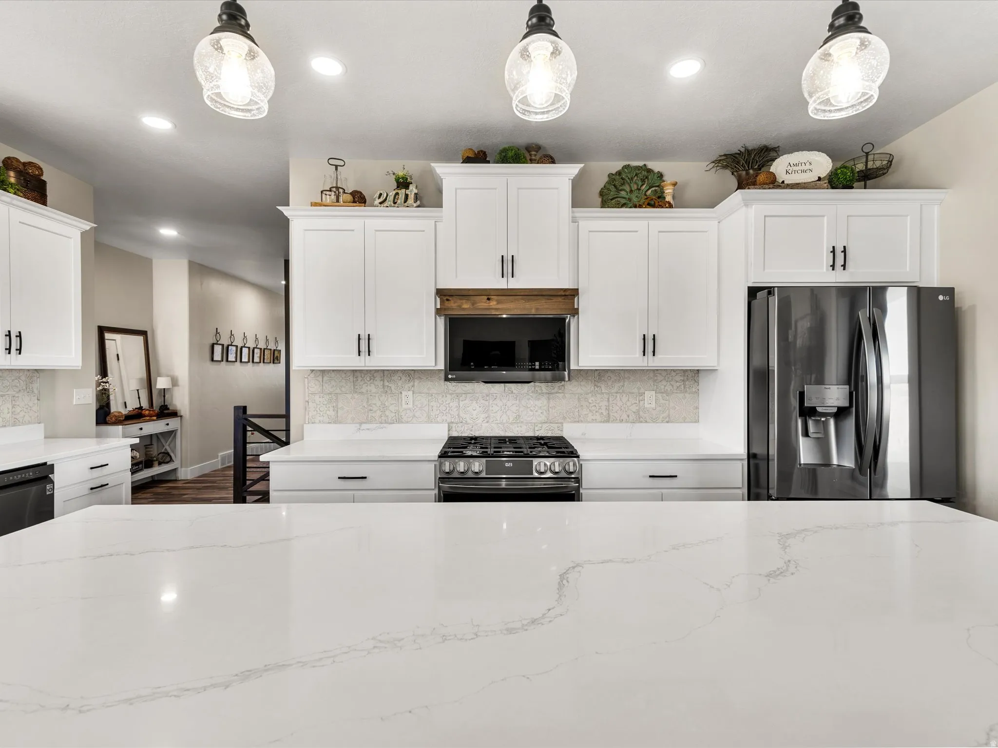 Spacious kitchen featuring an expansive island with a light-toned countertop, white cabinetry with dark hardware, a patterned backsplash, and stainless steel appliances