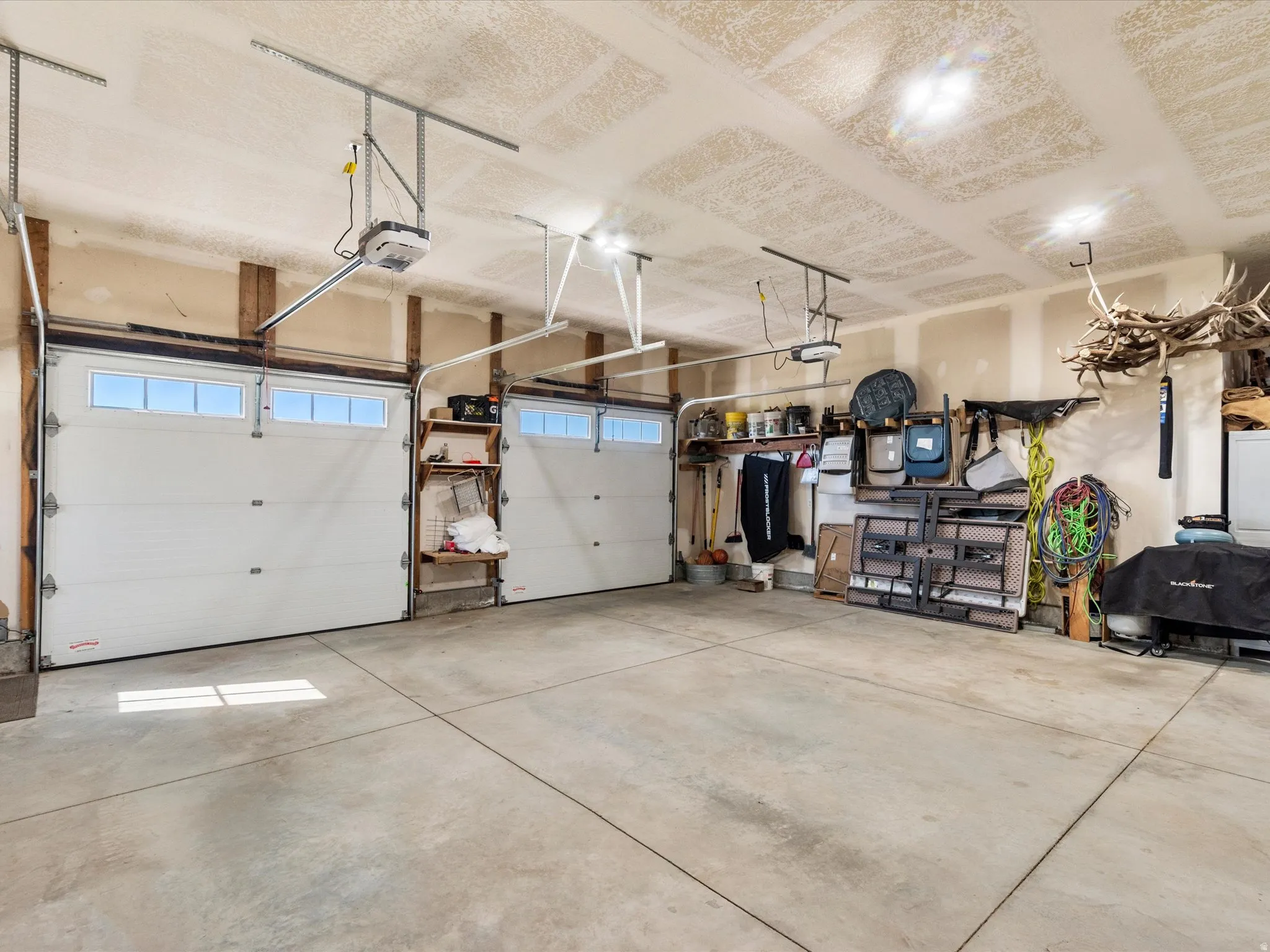 Two overhead garage doors with upper window panels, concrete flooring, and exposed wood structural beams