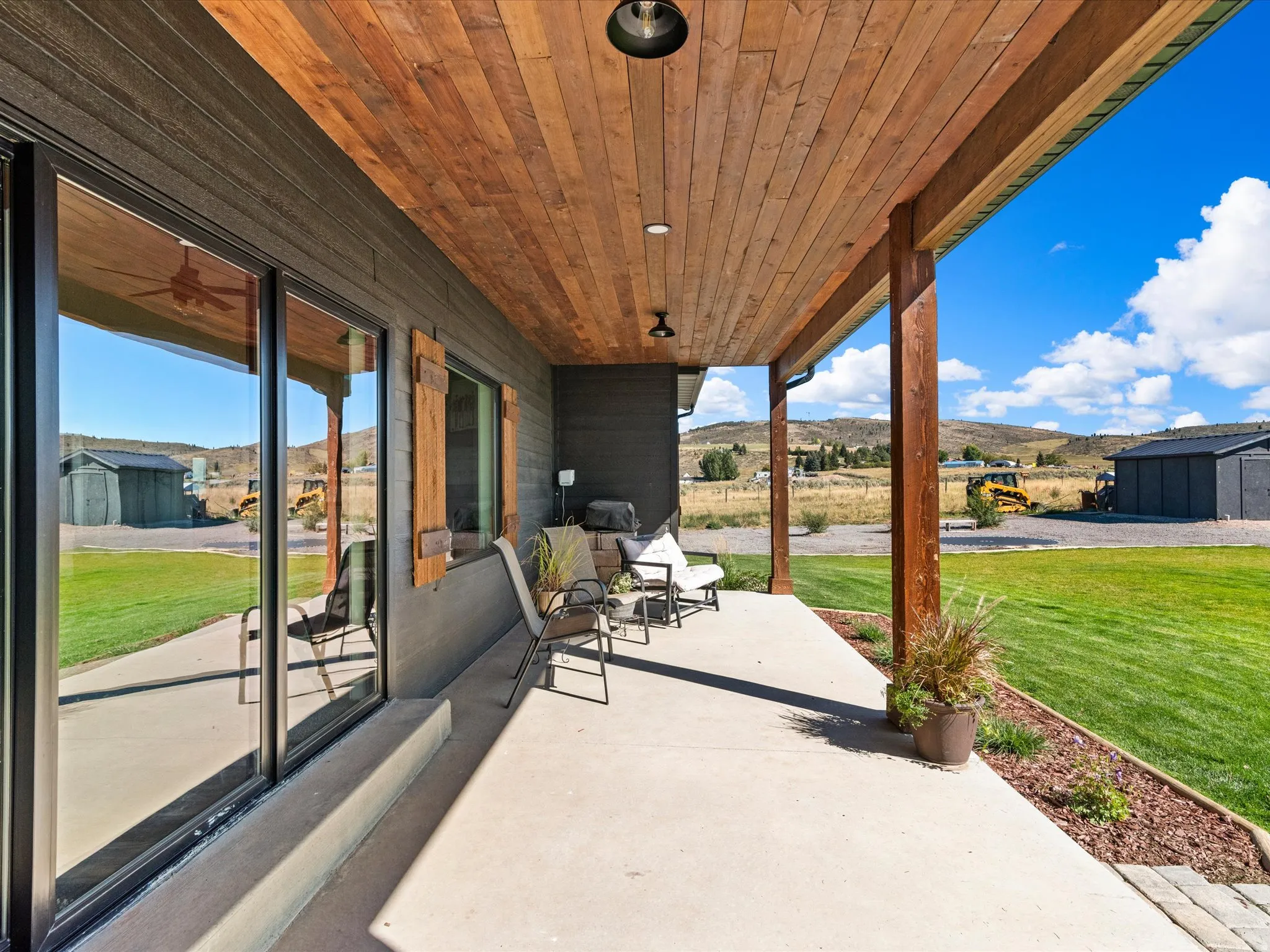 Covered concrete patio with wood-paneled ceiling, wood support columns, and dark exterior siding