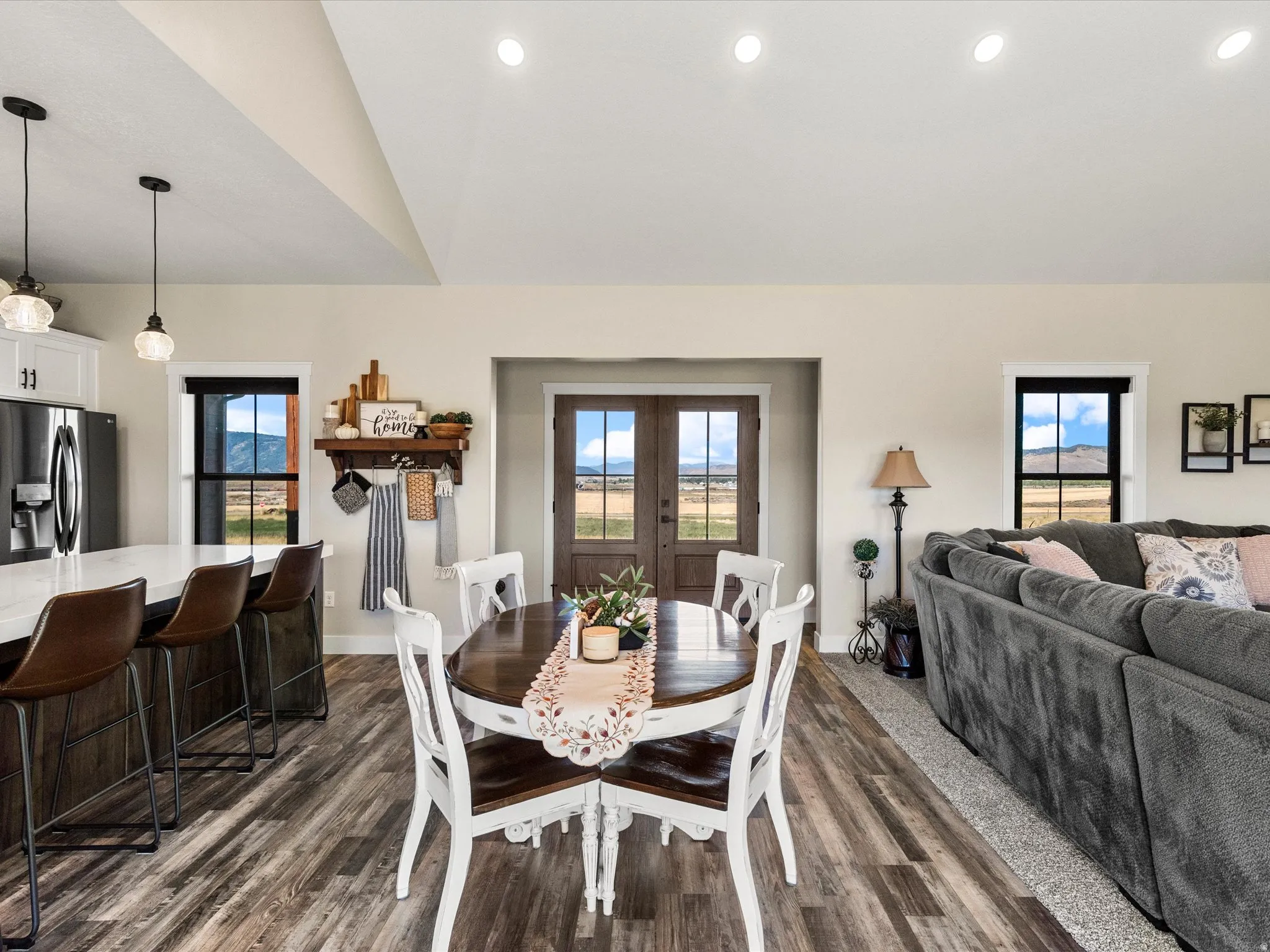 Vaulted ceiling with recessed lighting, wood-finish flooring, kitchen island with counter seating, double entry doors, and black-framed windows