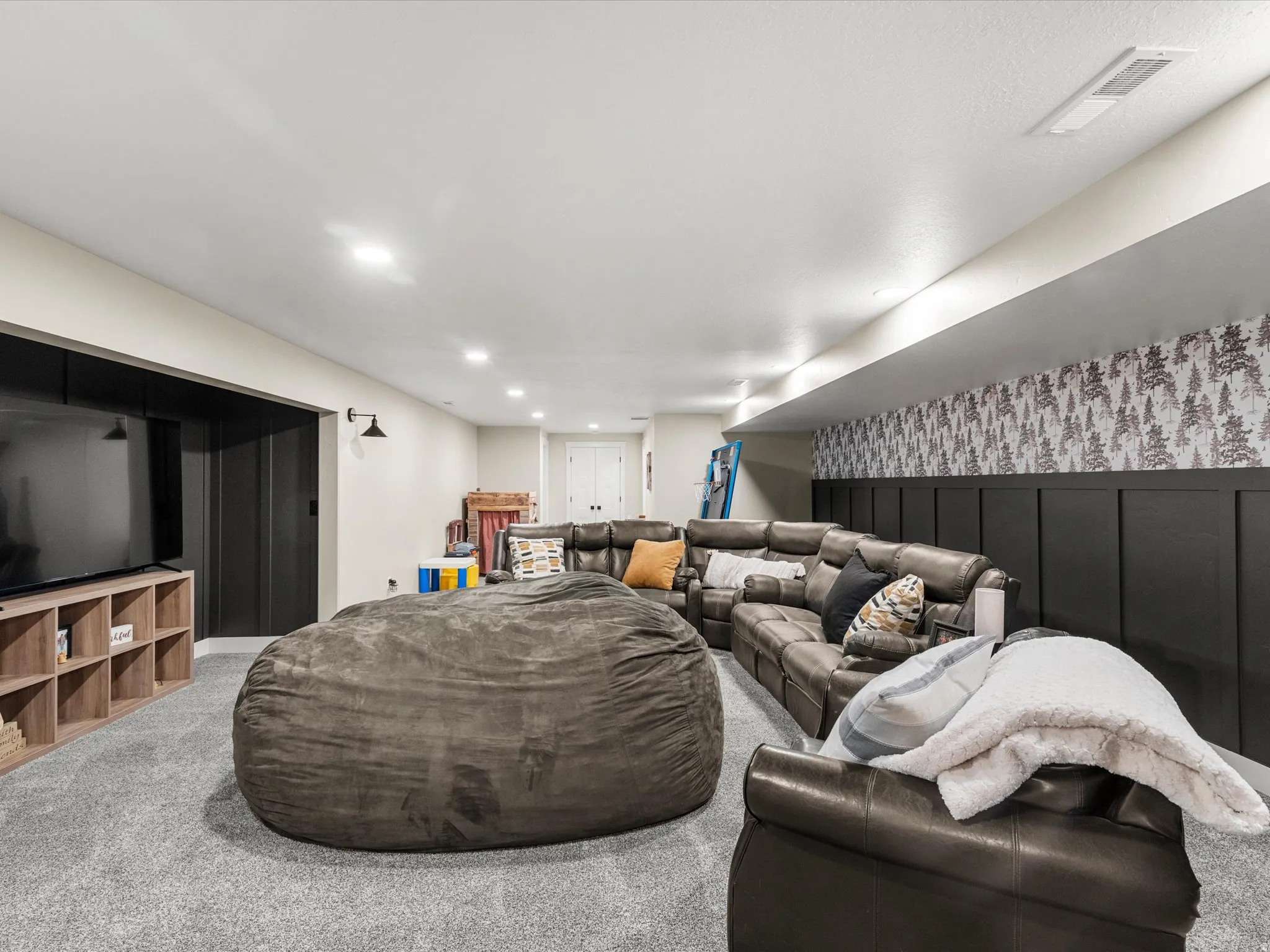 Recessed lighting, light gray carpeting, and a dark accent wall with board and batten paneling