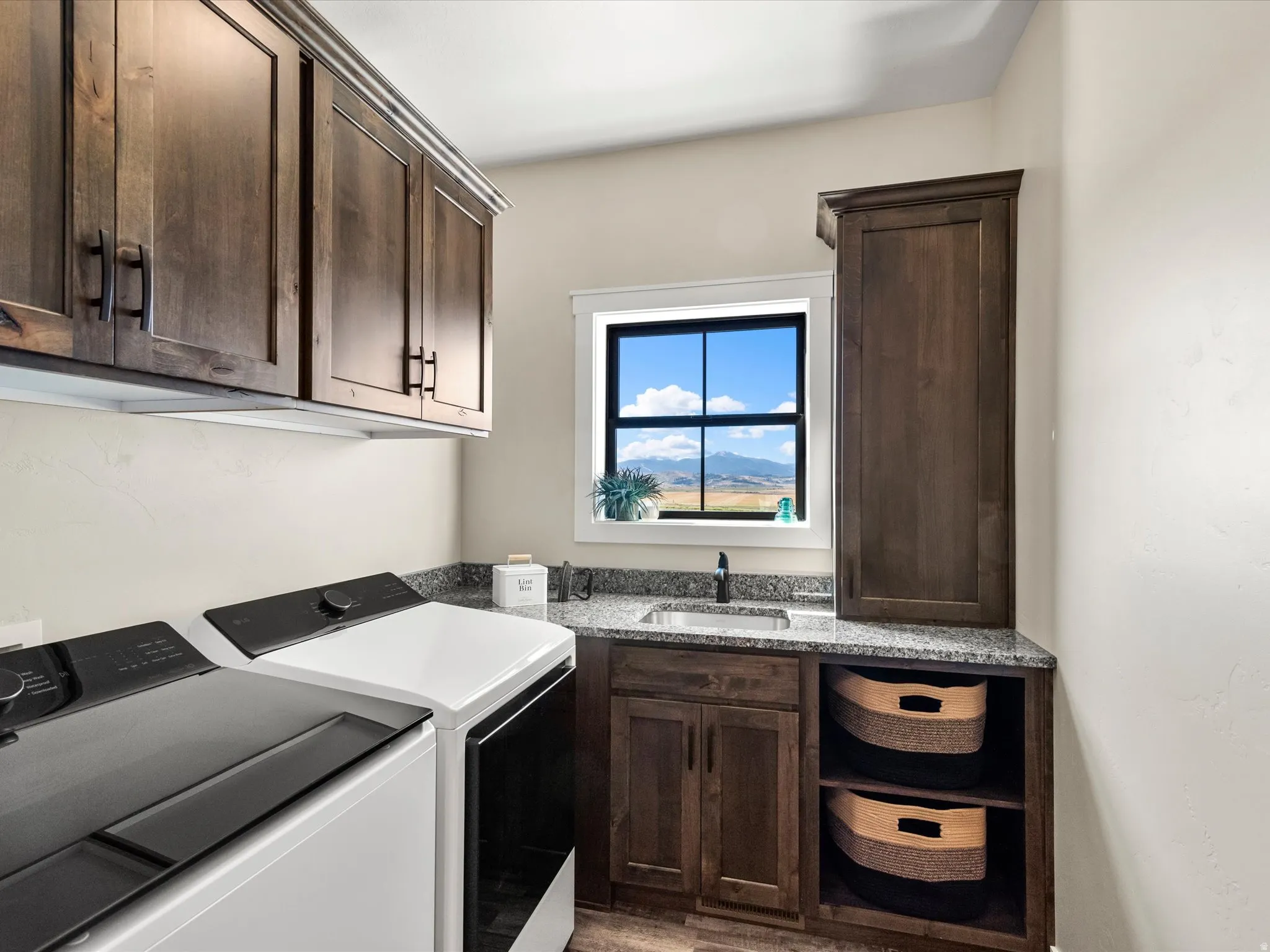 Dark wood-finish cabinetry, granite-style countertops, stainless steel sink with a dark-finish faucet, and an integrated window