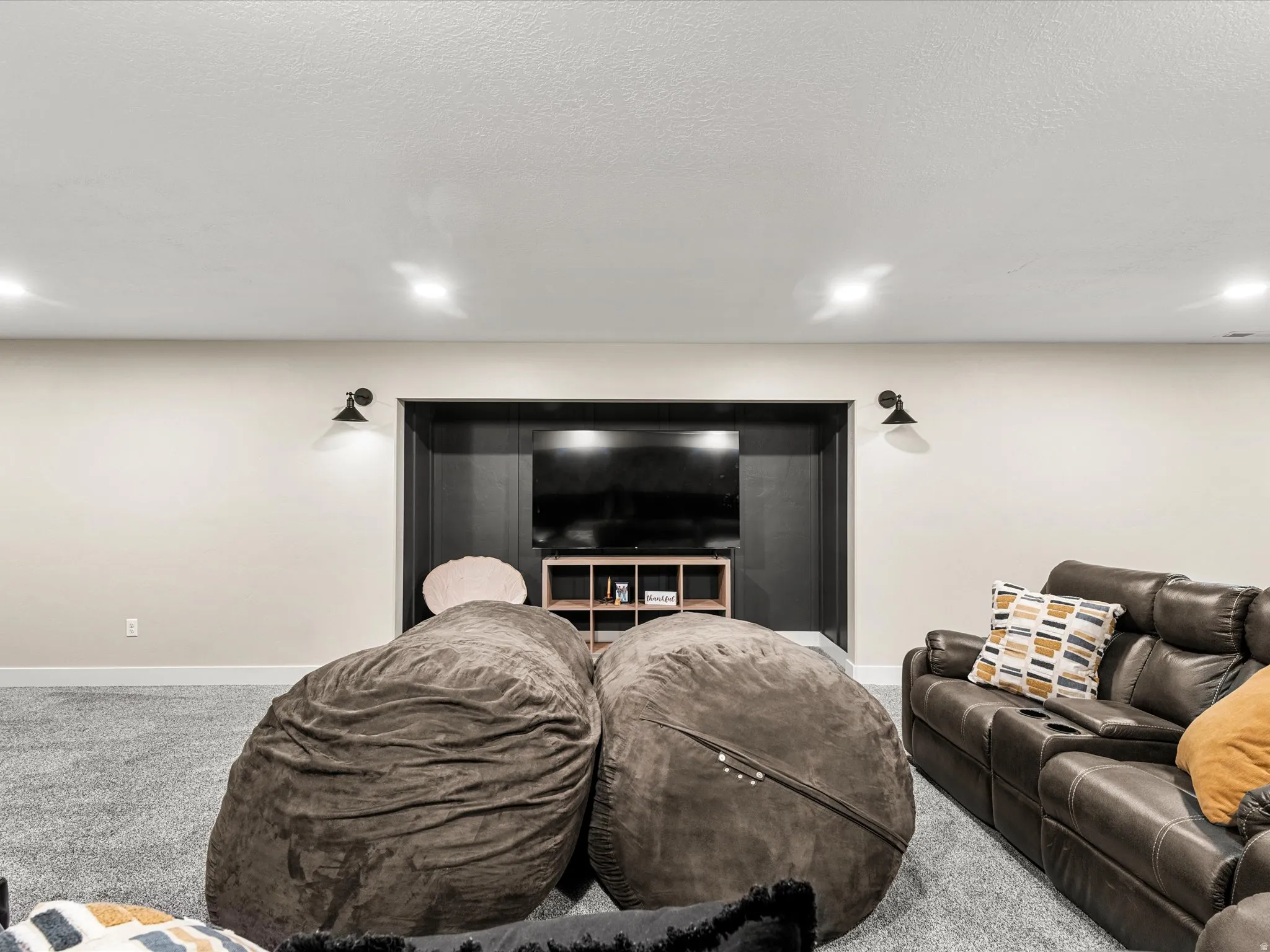 Recessed lighting illumination, wall-mounted sconces, light-toned walls, built-in media niche, carpeted flooring