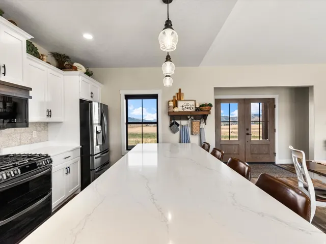 Expansive kitchen island with a light-toned countertop, white cabinetry with dark hardware, stainless steel refrigerator, and a gas range