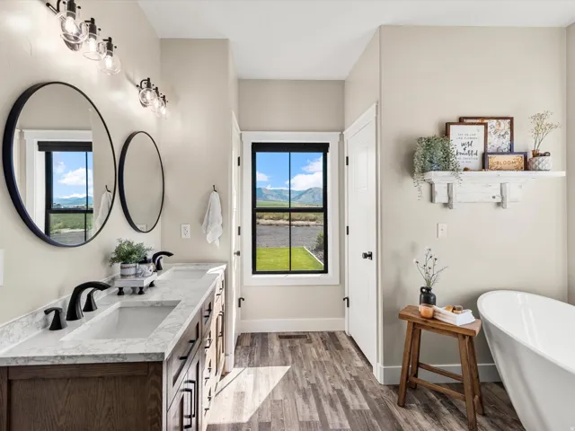 Dual vanity with undermount sinks and black fixtures, wood-finish flooring, freestanding bathtub, and a window with a black frame