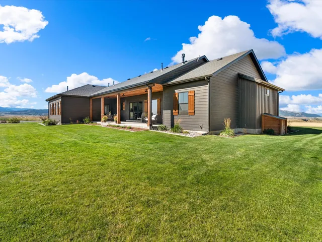 Expansive exterior featuring a covered patio with wood support beams, dark siding, and a vast lawn