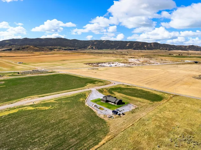 Expansive rural property featuring a gabled roof residence, surrounding agricultural fields, and distant mountain scenery