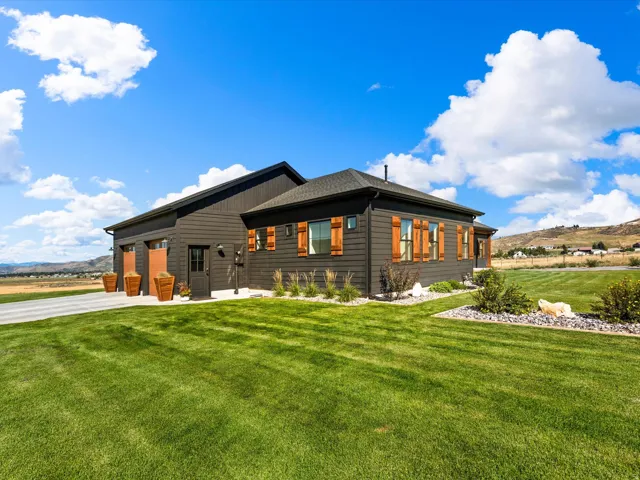 Dark-toned exterior siding with wood-tone window shutters, a two-car garage, and a gravel driveway