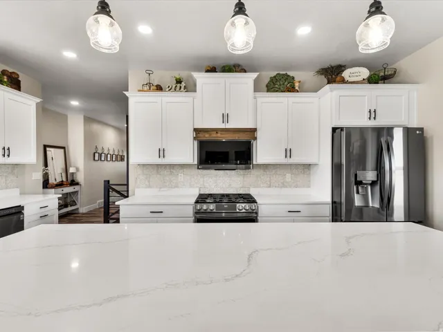 Spacious kitchen featuring an expansive island with a light-toned countertop, white cabinetry with dark hardware, a patterned backsplash, and stainless steel appliances