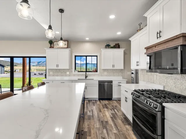 Spacious kitchen featuring an expansive island with a white countertop, white cabinetry with black hardware, stainless steel appliances, and wood-finish flooring