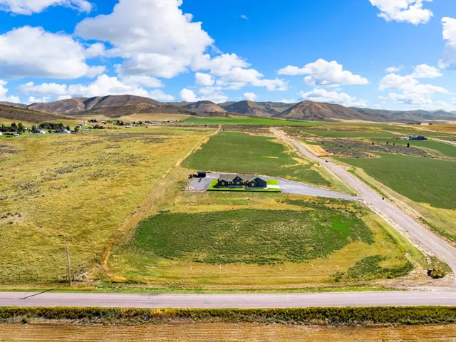 Expansive property featuring a single-story residence, gravel driveway, and surrounding open fields with distant mountains