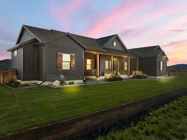 Board and batten siding, wood shutters, covered front porch with wood columns, landscaped beds, and a manicured lawn