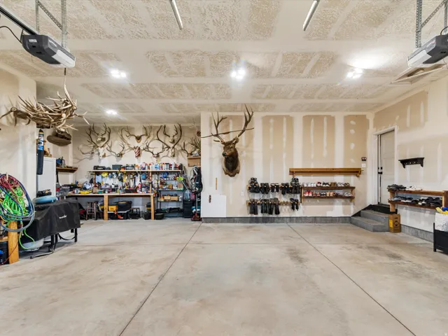 Expansive concrete floor garage with exposed ceiling joists, equipped with multiple overhead garage door openers, and a dedicated workspace featuring built-in shelving