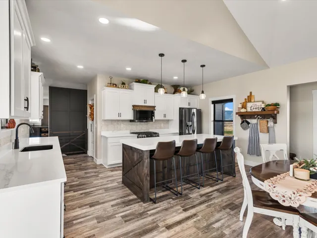 Spacious kitchen featuring white cabinetry, light-toned countertops, a dark wood-finish island with seating, wood-finish flooring, and a vaulted ceiling