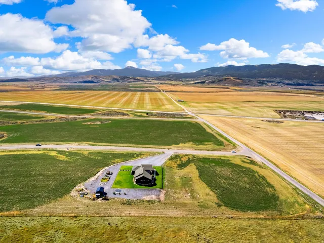 Expansive property featuring a residence with a dark-toned roof, surrounded by cultivated fields and distant mountains
