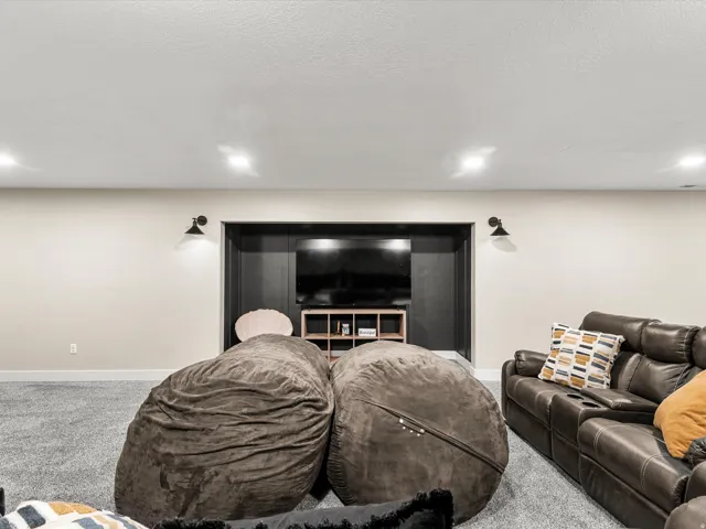 Recessed lighting illumination, wall-mounted sconces, light-toned walls, built-in media niche, carpeted flooring