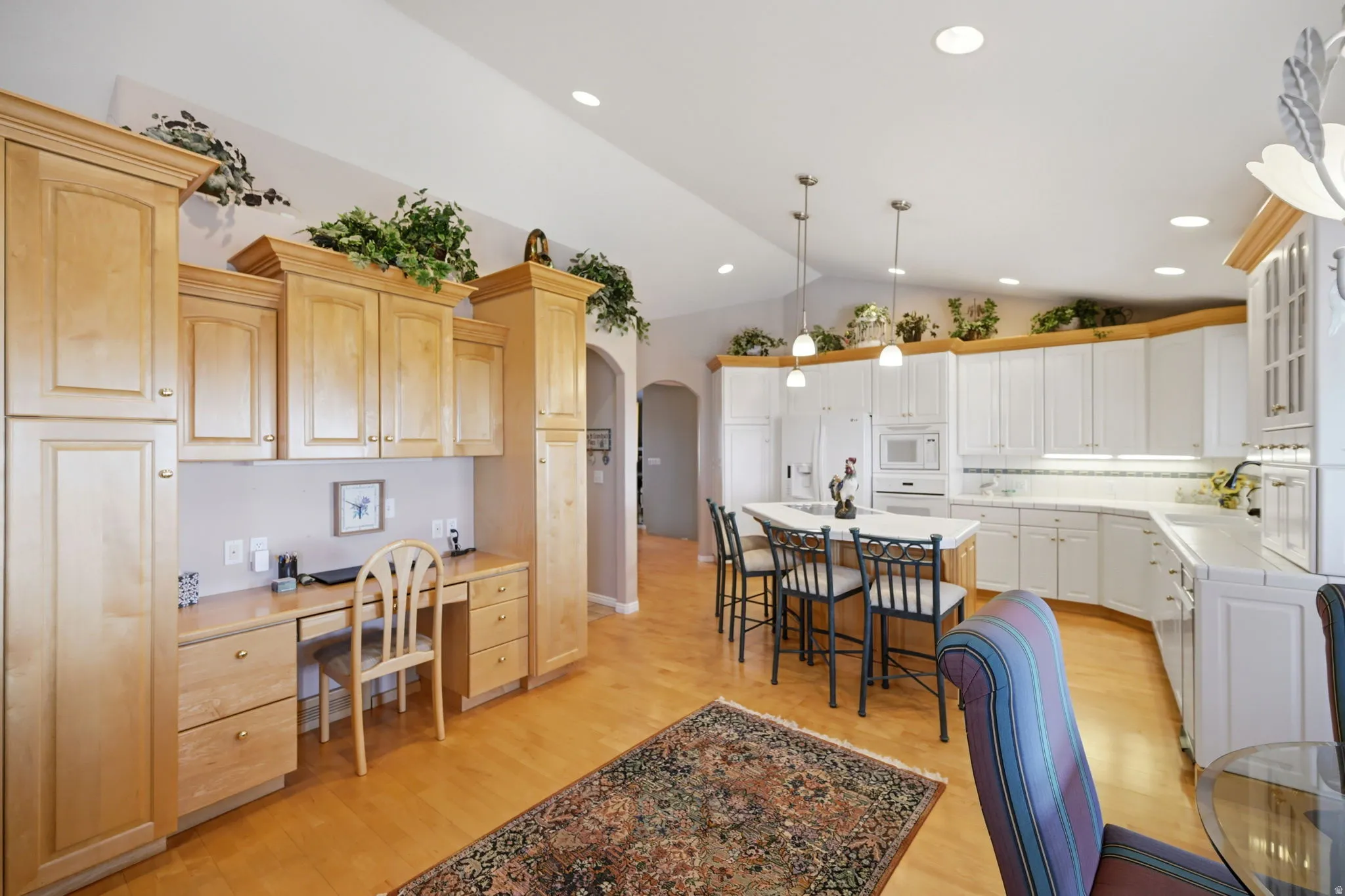 Expansive kitchen with a vaulted ceiling, recessed lighting, white cabinetry, a central island with pendant lighting, cabinetry with desk and light wood-finish flooring
