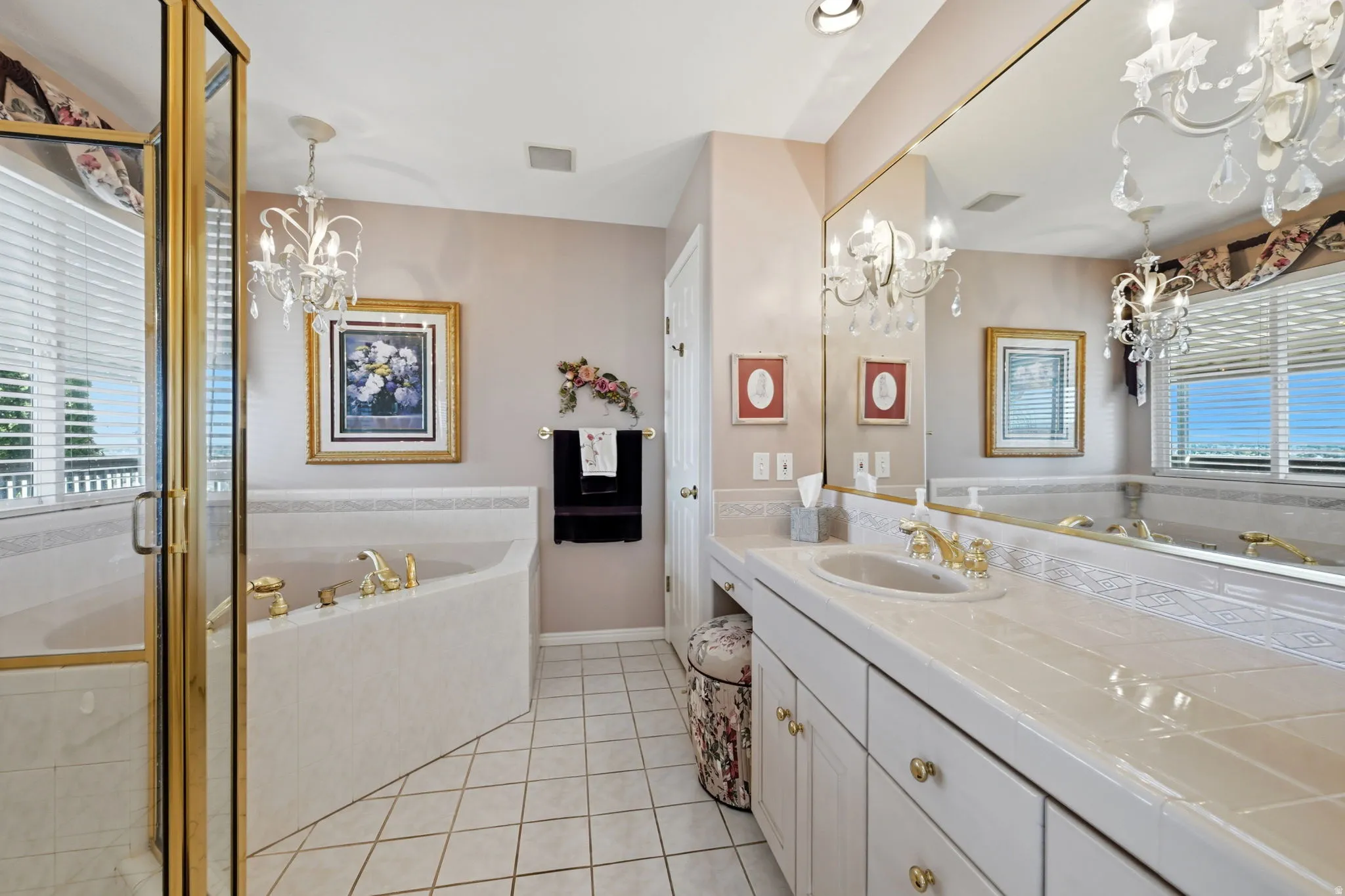 primary bathroom with tile countertop, integrated sink, large corner tub, walk-in shower, and gold-tone faucet