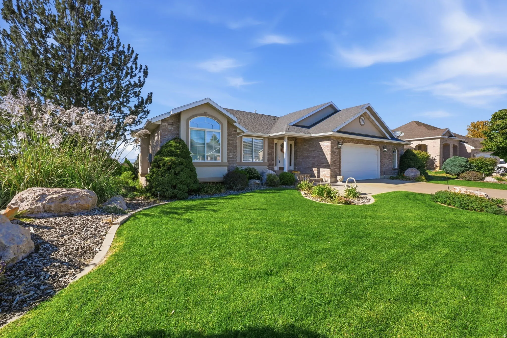 Brick exterior with a gabled roofline, arched window, attached garage, and manicured landscaping with decorative rocks