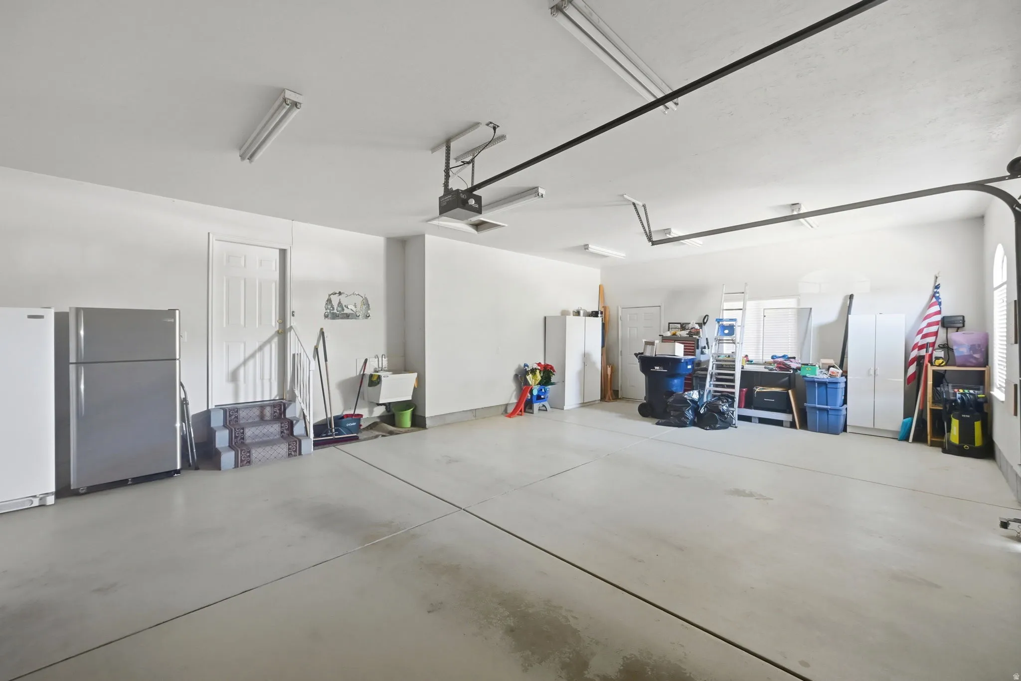 Spacious garage with high ceilings, garage sized extra space for storage, multiple fluorescent light fixtures, and a utility sink